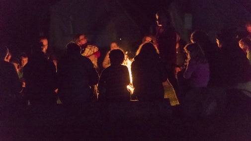 A group gathered around a fire in the dark listening to a story